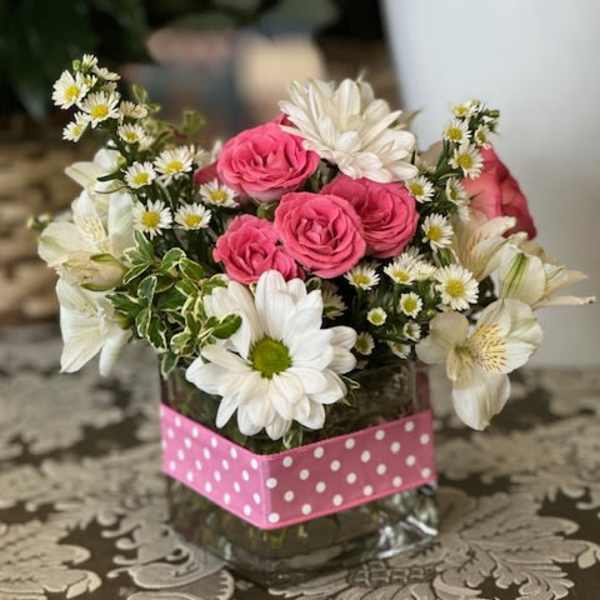 Pink roses and white daisies arranged in a glass vase with a pink polka-dot wrap