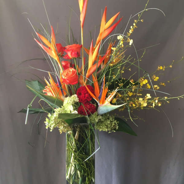 Tall tropical arrangement with orange birds of paradise and red roses in a glass vase