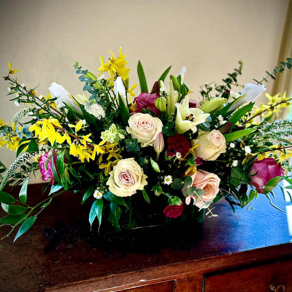 Low centerpiece of ivory roses, white lilies, yellow blooms and pink flowers in a black rectangular vase
