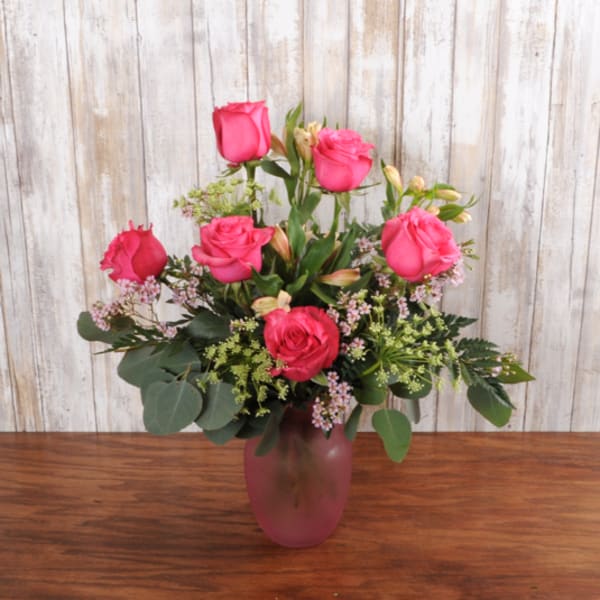 Pink rose bouquet with filler flowers in a frosted pink glass vase on a wooden table