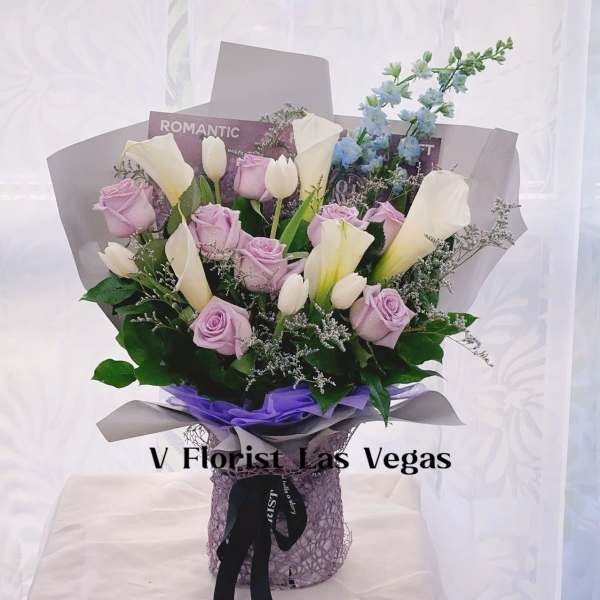 Arrangement of lavender roses, white tulips, and calla lilies in wrapped bouquet with purple accents