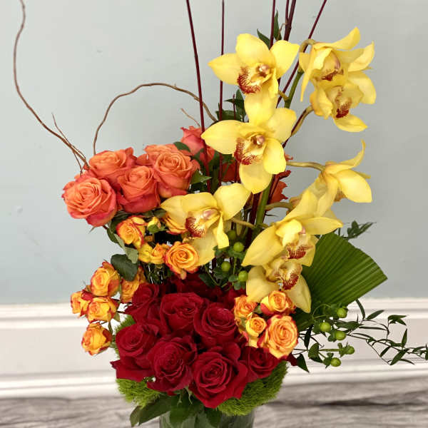 Red roses and yellow orchids in a tall glass vase