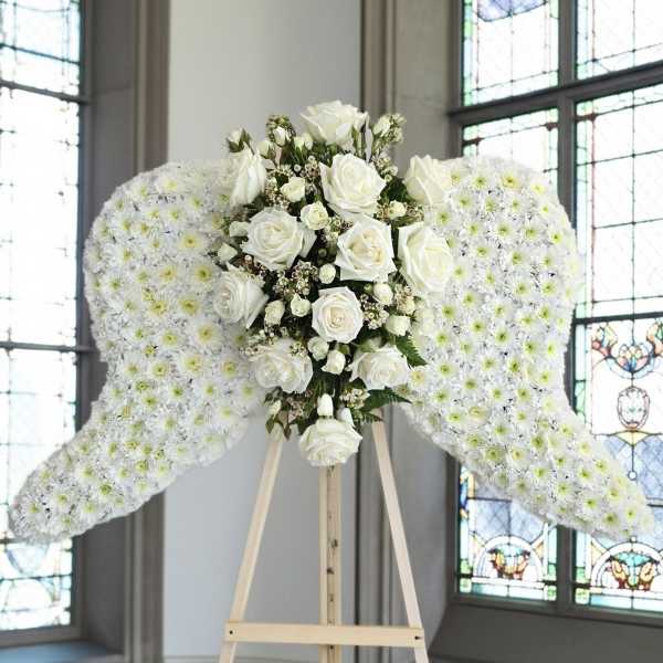 White floral angel wings on a wooden stand with roses in the center