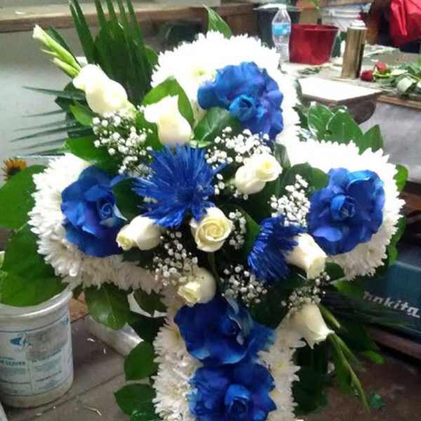 Standing cross-shaped funeral arrangement with blue and white flowers on an easel