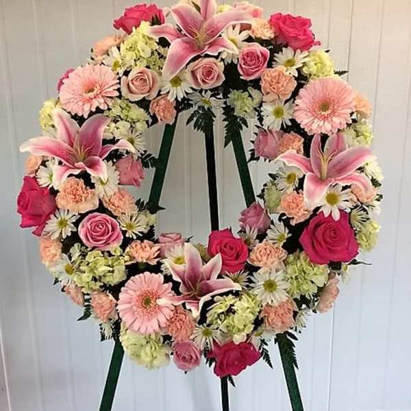 Heart-shaped floral wreath on a stand with pink lilies, roses, daisies, and carnations