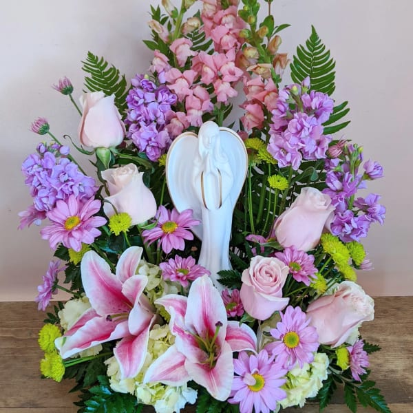 Pink and purple floral arrangement with lilies and roses around a white angel figurine