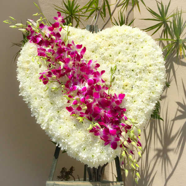 Heart-shaped white floral arrangement with a magenta orchid spray