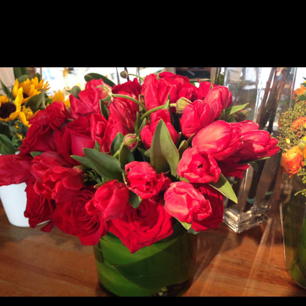 Red tulips and roses arranged in a green glass vase
