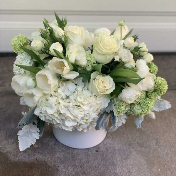 White floral arrangement in a round white vase with green accents