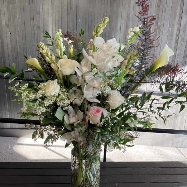 Tall floral arrangement in a glass vase with white orchids and roses