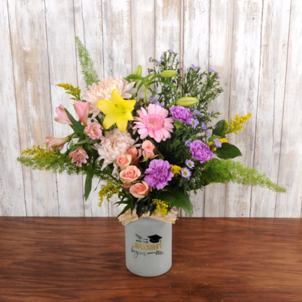 Mixed bouquet of pink, purple, and yellow flowers in a white graduation-themed jar vase