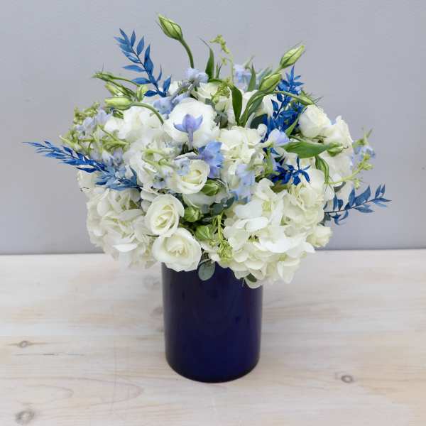 White and light blue flower arrangement in a dark blue cylinder vase