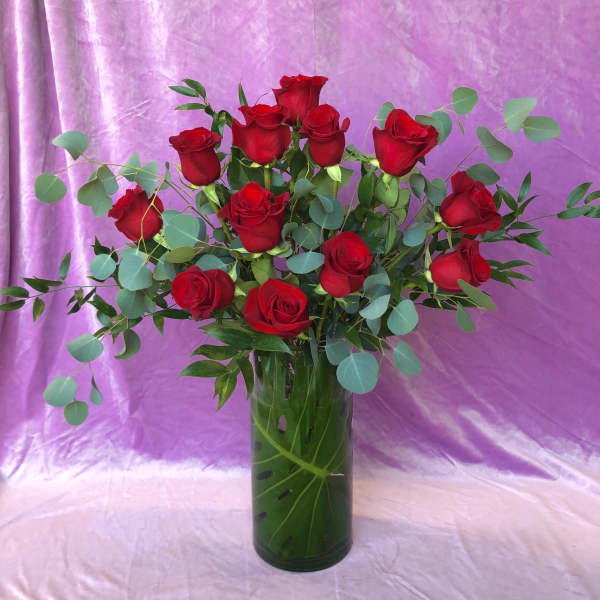 Red roses in a tall glass vase with eucalyptus foliage