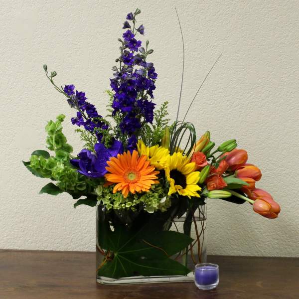 Mixed bouquet with sunflowers, gerbera daisies, tulips, and purple blooms in a glass vase