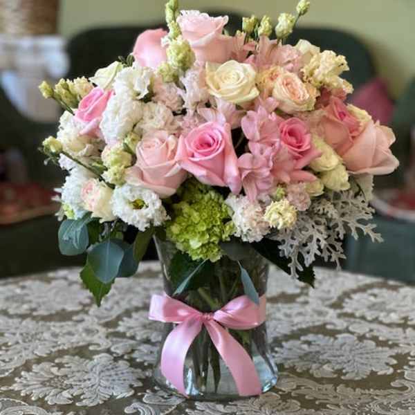 Pink and white rose bouquet in a glass vase with a pink ribbon