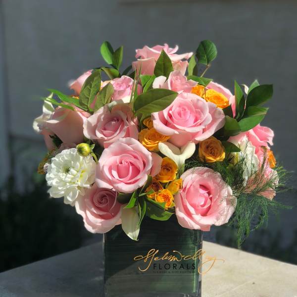 Pink and yellow rose arrangement in a dark square vase