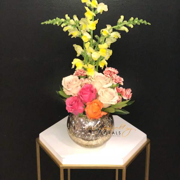 Tall floral arrangement with roses, carnations, and yellow snapdragons in a mirrored vase