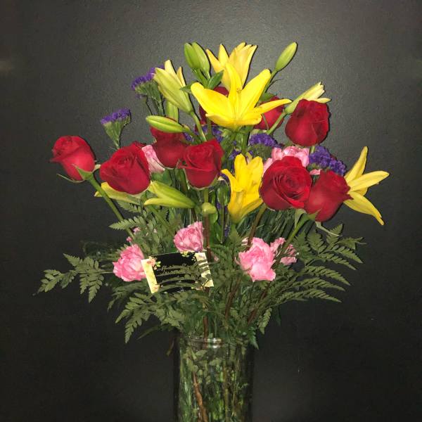 Bouquet of red roses and yellow lilies in a tall glass vase
