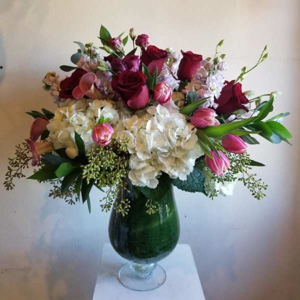 Bouquet of red roses, pink tulips, and white hydrangeas in a green glass vase