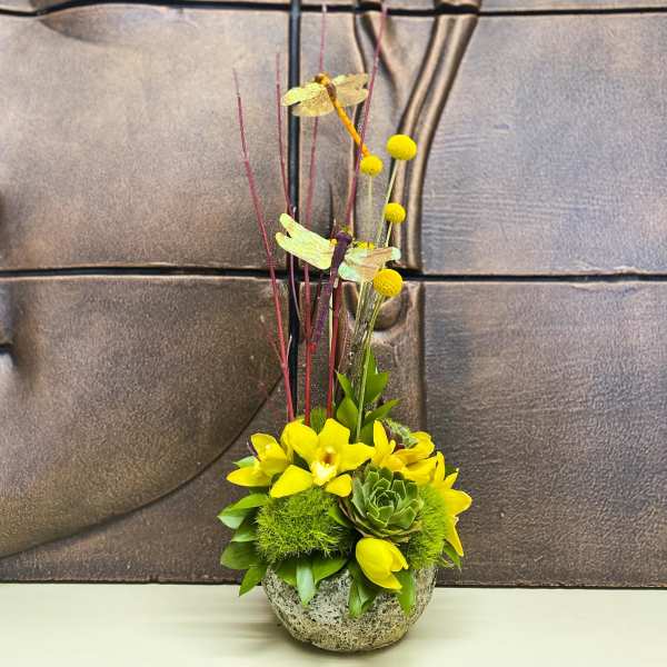 Yellow floral arrangement in a round stone bowl with tall decorative stems