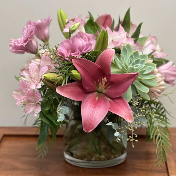Pink lilies and mixed pink flowers in a glass vase with a succulent accent