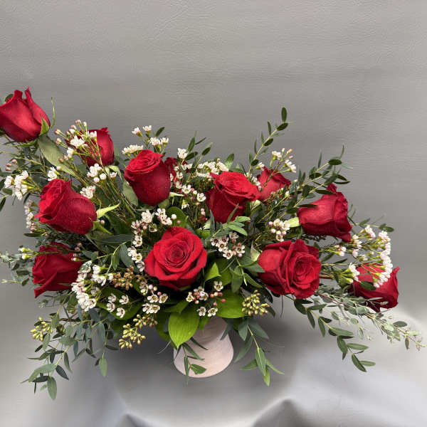 Red roses arranged in a low white vase with small white filler flowers
