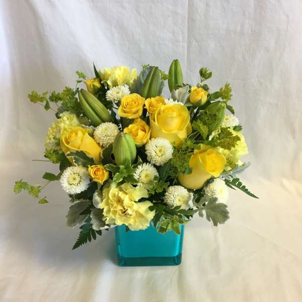 Yellow roses and white pom flowers in a turquoise vase