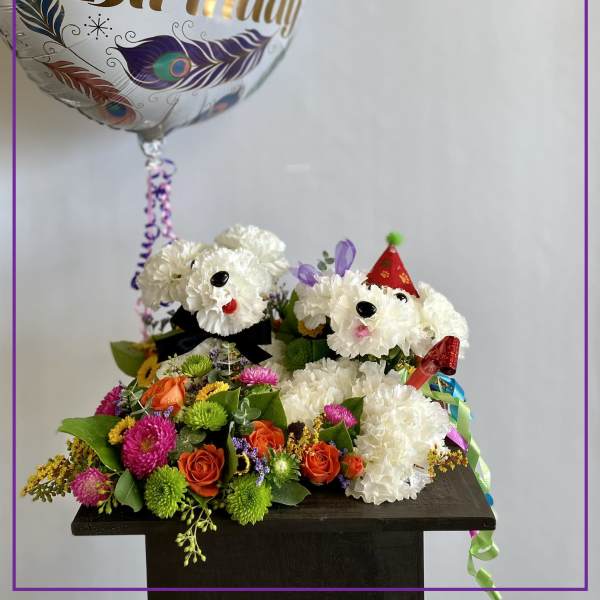 Birthday balloon above a flower arrangement with two white dog faces