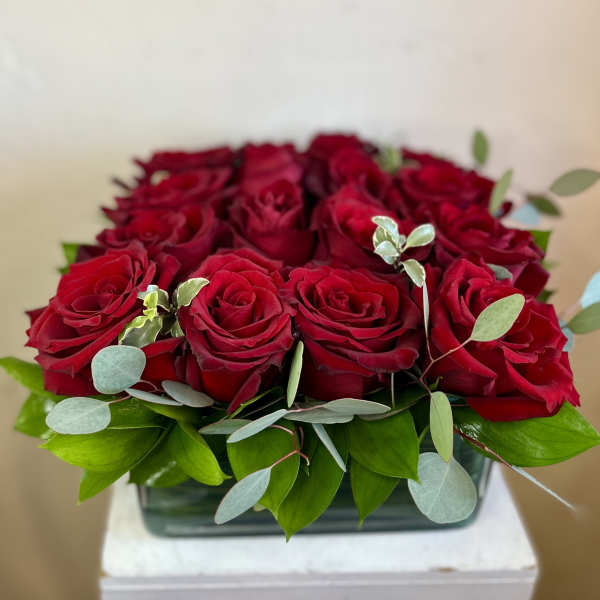 Red roses arranged in a low rectangular vase with green foliage