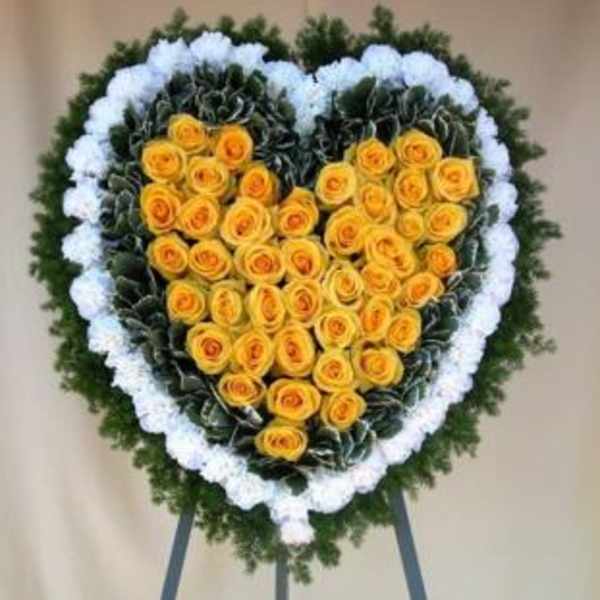 Heart-shaped floral wreath with yellow roses and white edging on an easel