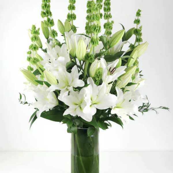 White lilies and green spikes arranged in a tall glass vase