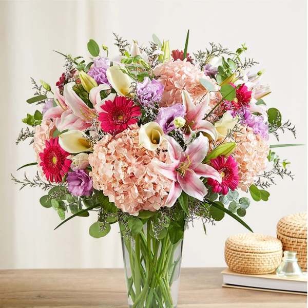 Mixed bouquet of pink lilies, hydrangeas, gerbera daisies, and calla lilies in a glass vase