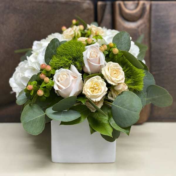 White roses and green pom-pom flowers in a white square vase