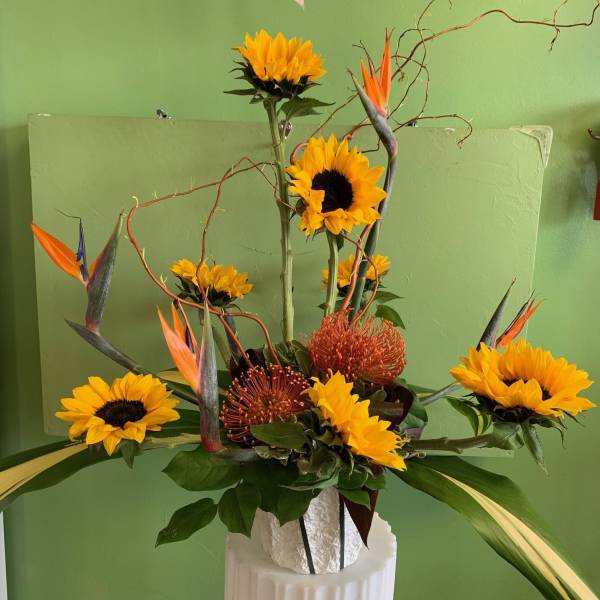 Tall floral arrangement with sunflowers and orange bird-of-paradise in a white vase