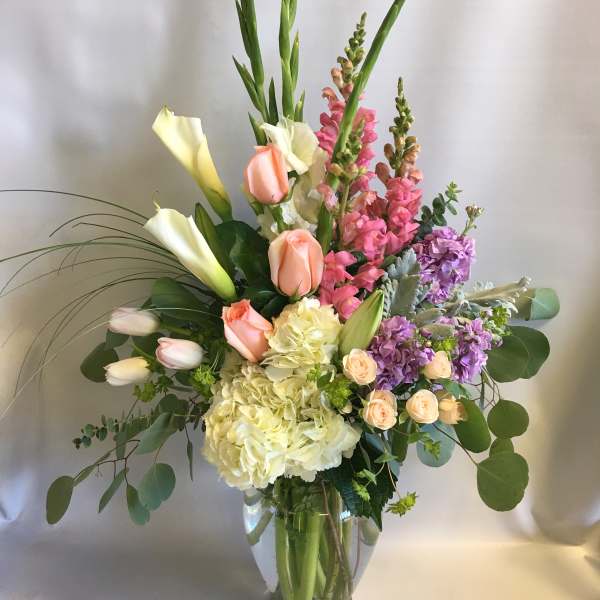 Tall mixed bouquet with calla lilies, roses, hydrangeas, and snapdragons in a glass vase