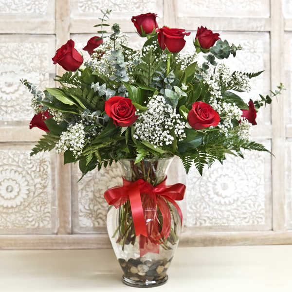 Red roses and baby's breath in a clear glass vase with a red ribbon