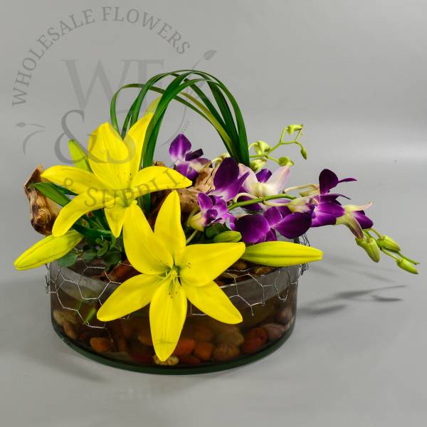 Yellow lilies and purple orchids in a glass bowl with stones