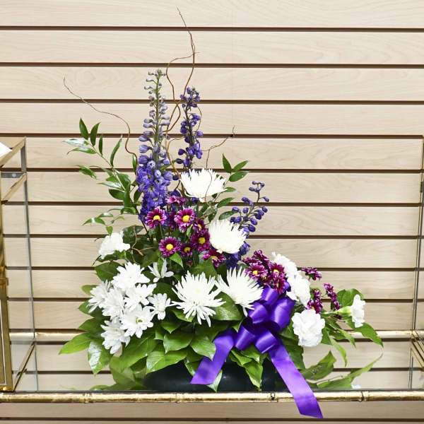 Purple and white floral arrangement with a satin ribbon in a low container