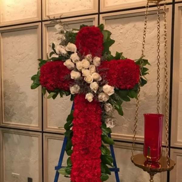 Red floral cross on a stand with white roses and greenery
