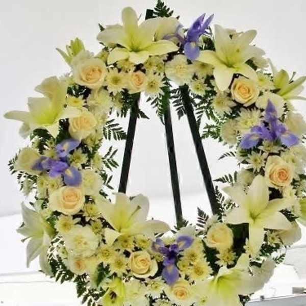 Floral wreath with pale lilies, cream roses, and purple accents on a black stand
