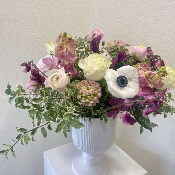 Mixed pink and white flowers arranged in a white pedestal vase