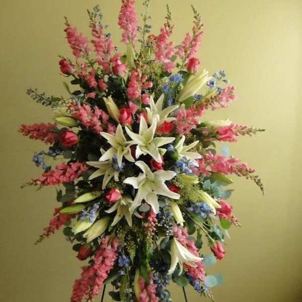 Tall floral spray with white lilies, pink blooms, and blue accents on a stand