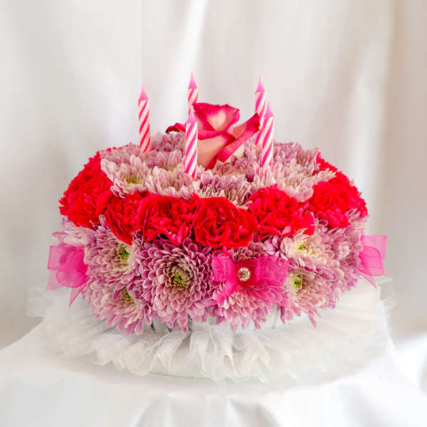 Round pink and red floral cake with striped candles and a rose topper
