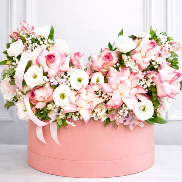 Pink and white roses arranged in a round pink box with ribbon