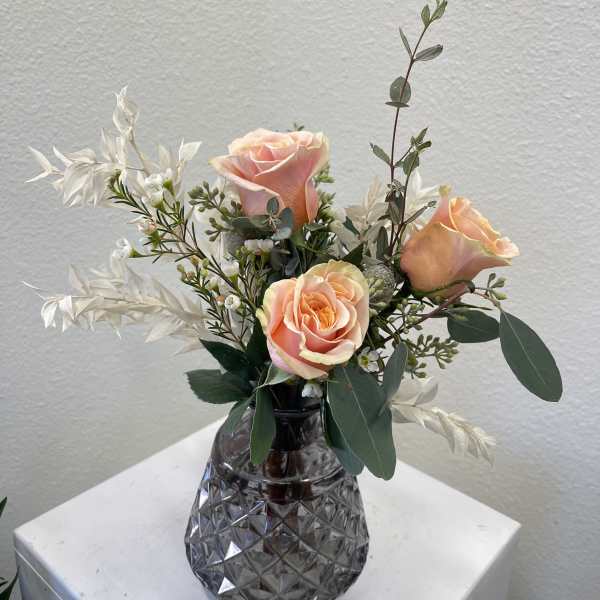 Peach roses in a dark glass vase with white filler flowers