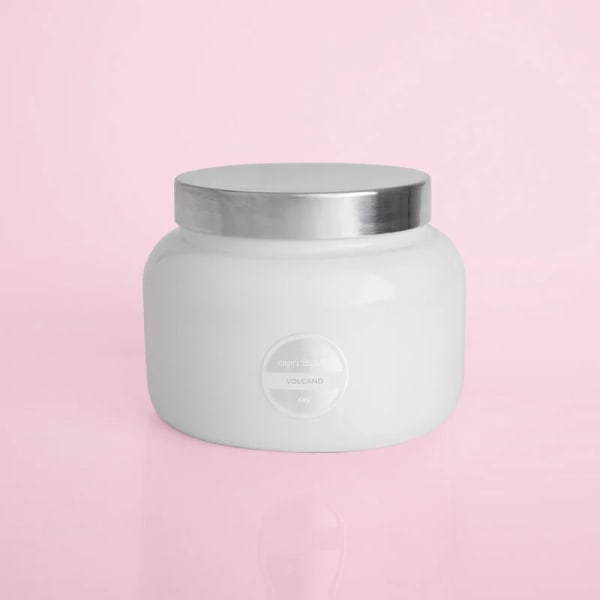 White candle jar with a silver lid on a pink background