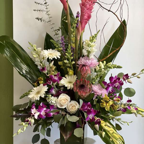 Tall mixed floral arrangement with pink tropical blooms and orchids in a vase