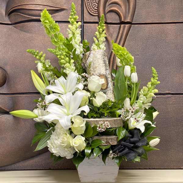 White lilies and roses arranged in a rustic planter with green spikes.