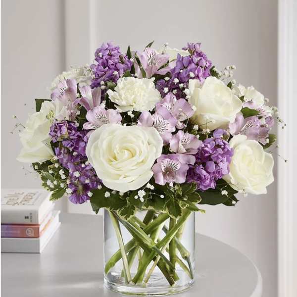 White roses and purple flowers arranged in a clear glass vase