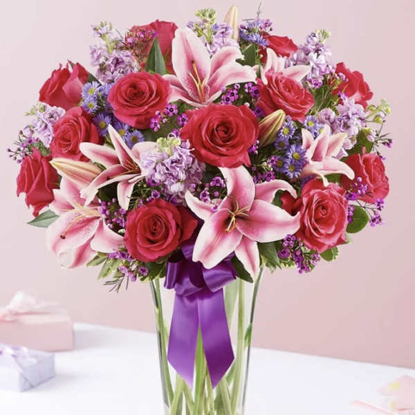 Pink roses and lilies arranged in a clear glass vase with a purple ribbon